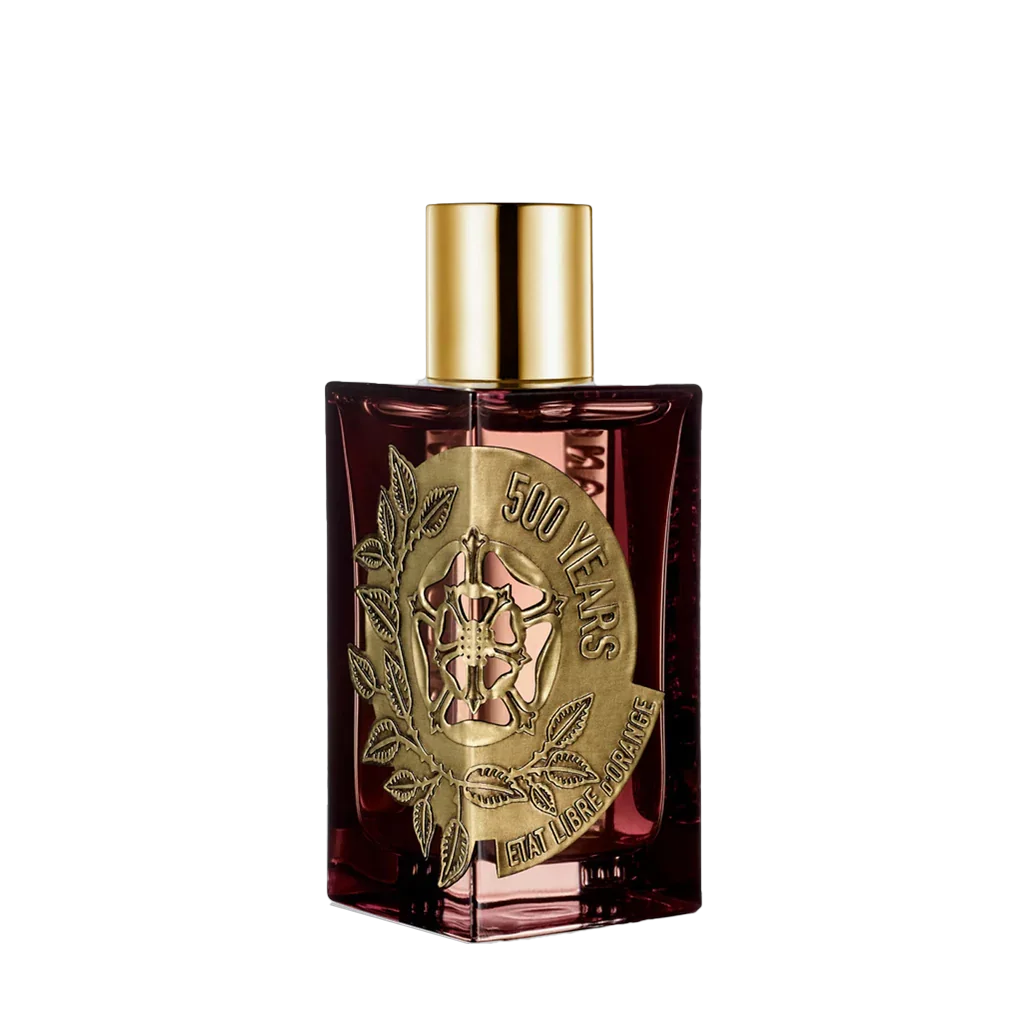 Parfümflasche mit rechteckigem, transparentem rotem Glas, Messingverzierung mit "500 Years" und markantem Logo. Goldfarbener Sprühkopf. Produkt: 500 Years von Etat Libre D'Orange.