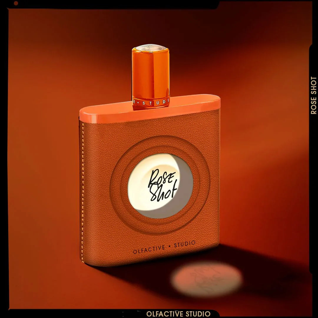 Parfümflakon "Rose Shot" von Olfactive Studio, mit orangefarbenem Verschluss und braunem Ledergehäuse.