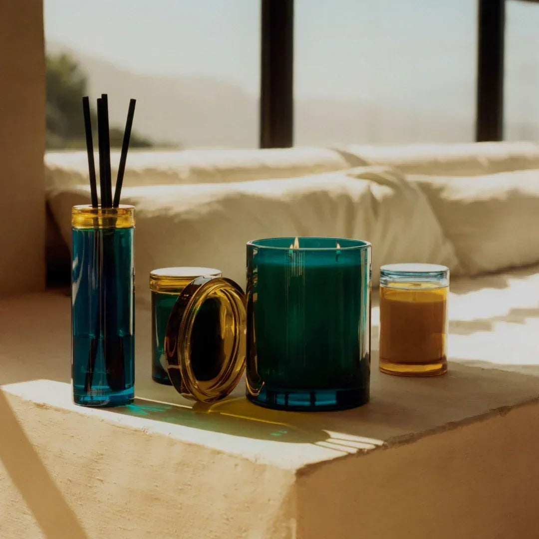 Ein Set von Glasdiffusor und Kerzen in verschiedenen Größen in Blau und Gelb. Titel: Sunseeker Diffuser. Anbieter: Paul Smith.