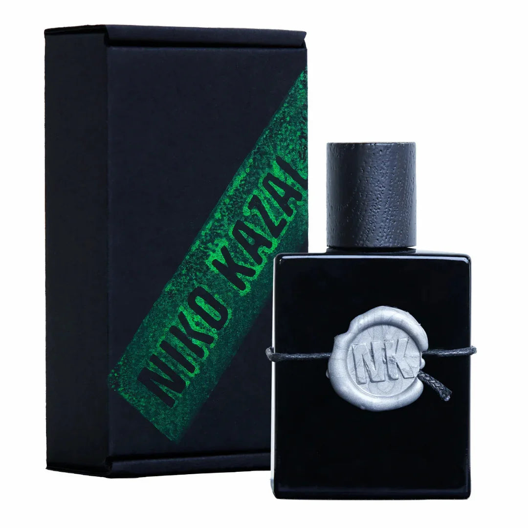 Schwarzes rechteckiges Parfümfläschchen mit silbernem Siegel und schwarzem Verschluss, daneben schwarze Verpackungsbox mit grünem NIKO KAZAL Schriftzug. Produkt: WHITE BLESSING 20%, Anbieter: Niko Kazal.