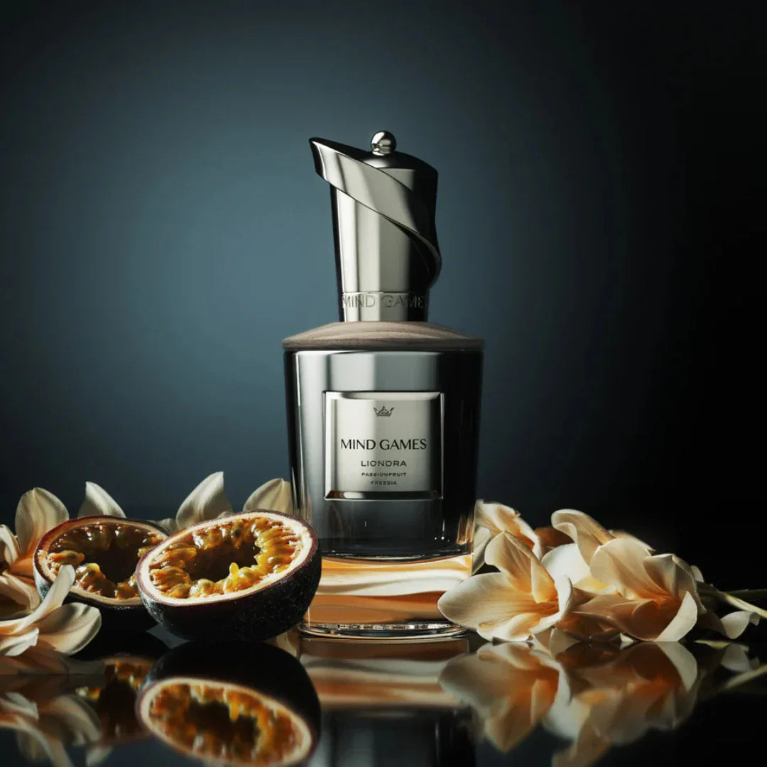 Parfümflasche "Lionora" von Mind Games, umgeben von geschnittenen Passionsfrüchten und weißen Blüten.
