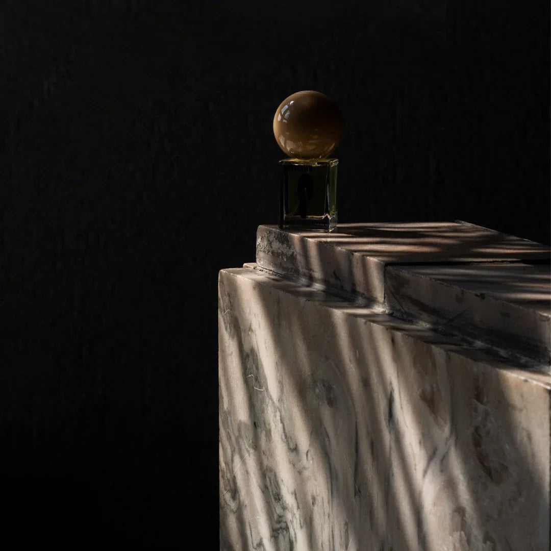Parfümflakon "Moonmilk" von Stora Skuggan auf einem marmorgefärbten Tisch. Runder, brauner Verschluss.
