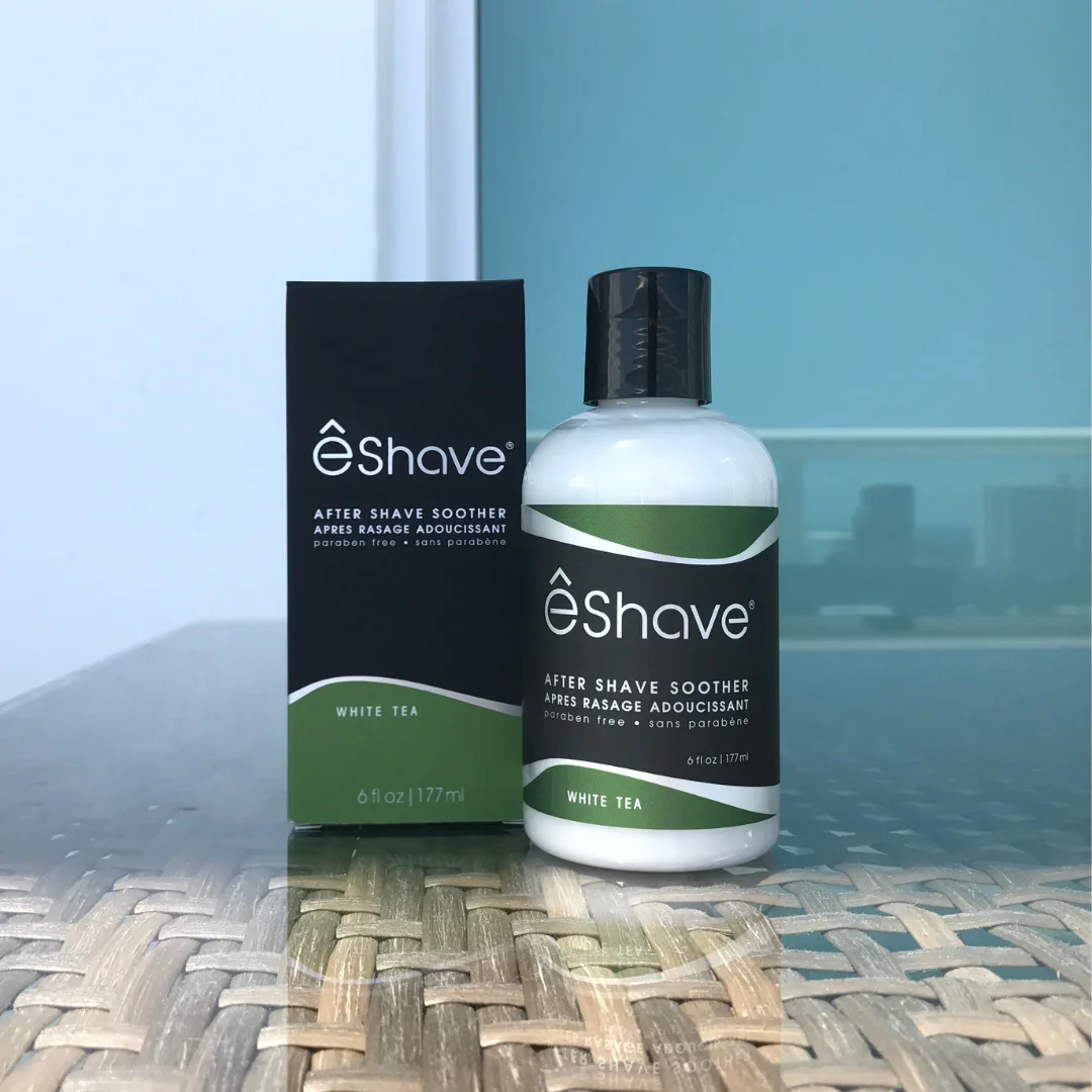 Die Lotion "White Tea" von eShave. Die Flasche ist weiß mit schwarzem Etikett und schwarzem Verschluss neben einer schwarzen Schachtel.
