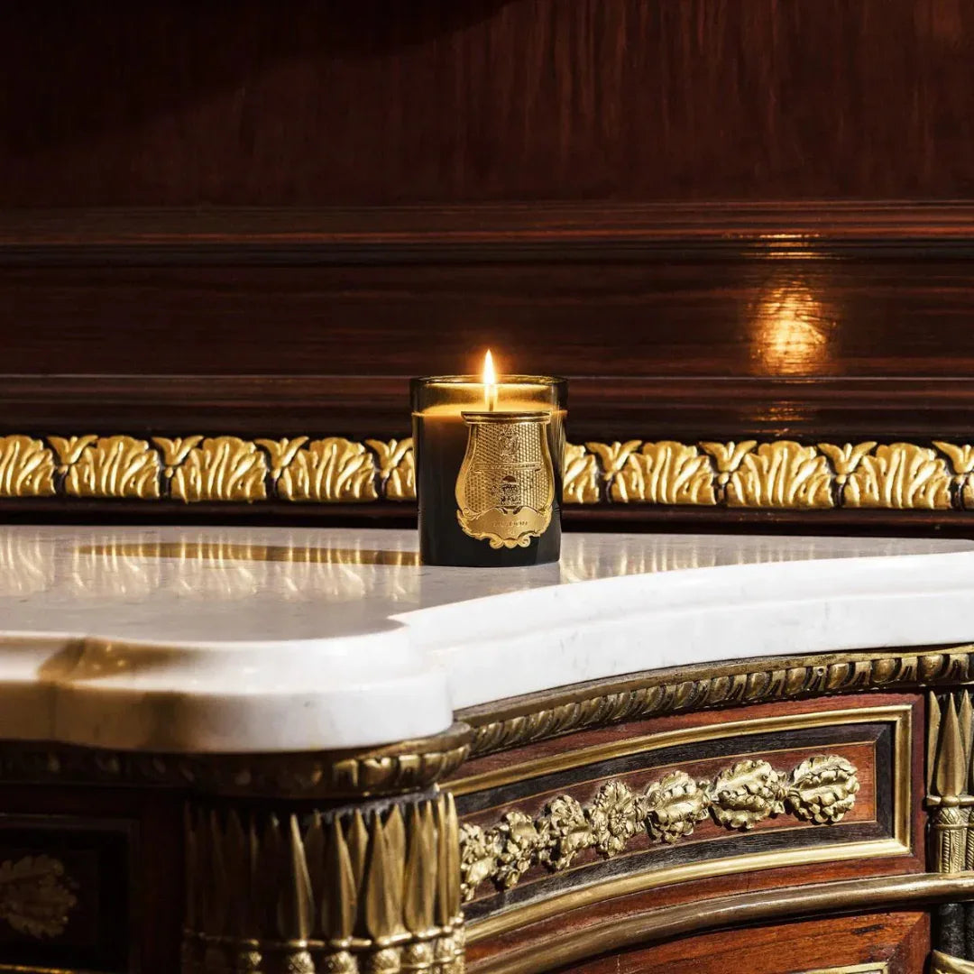 Duftkerze "GABRIEL" von Trudon, schwarze Glasdose mit goldenem Emblem und brennender Flamme auf einem Marmortisch.