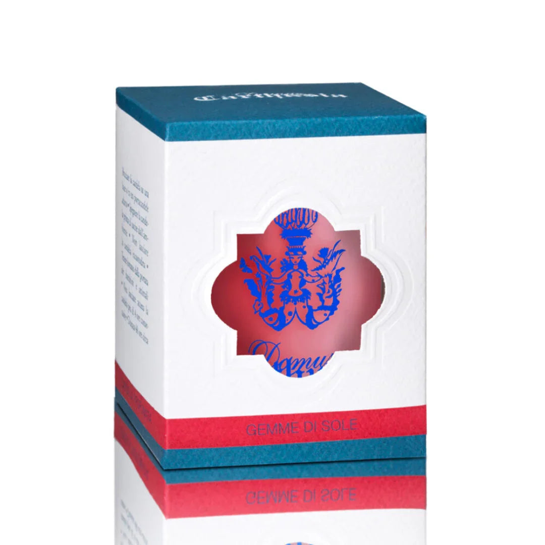 Quadratische Verpackung der Gemme di Sole Duftkerze von Carthusia, mit einem Sichtfenster und blauem Wappenmotiv.