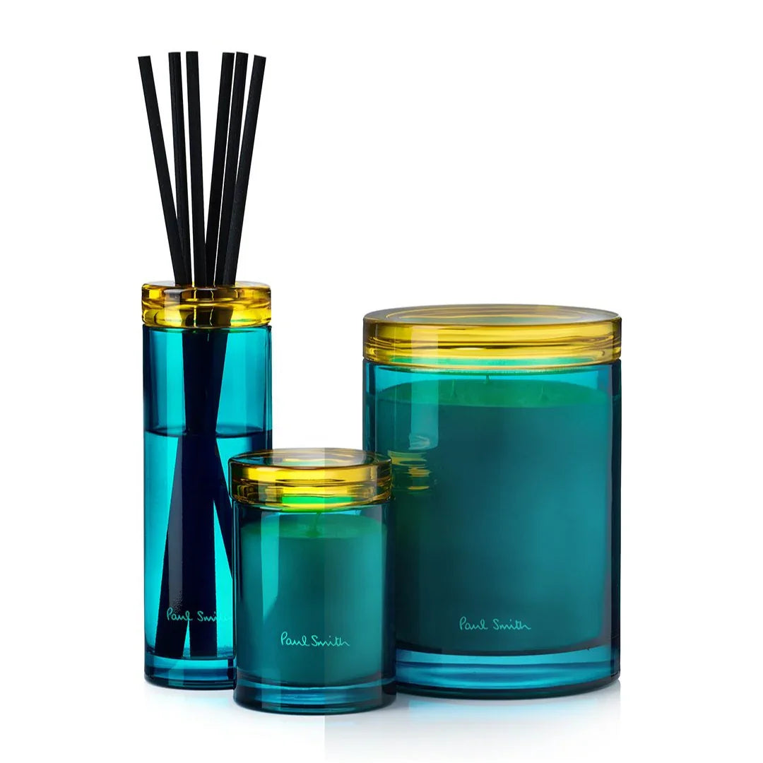 Der Sunseeker Diffuser von Paul Smith. Glasflasche mit blauen und gelben Details, gefüllt mit schwarzen Duftstäbchen.