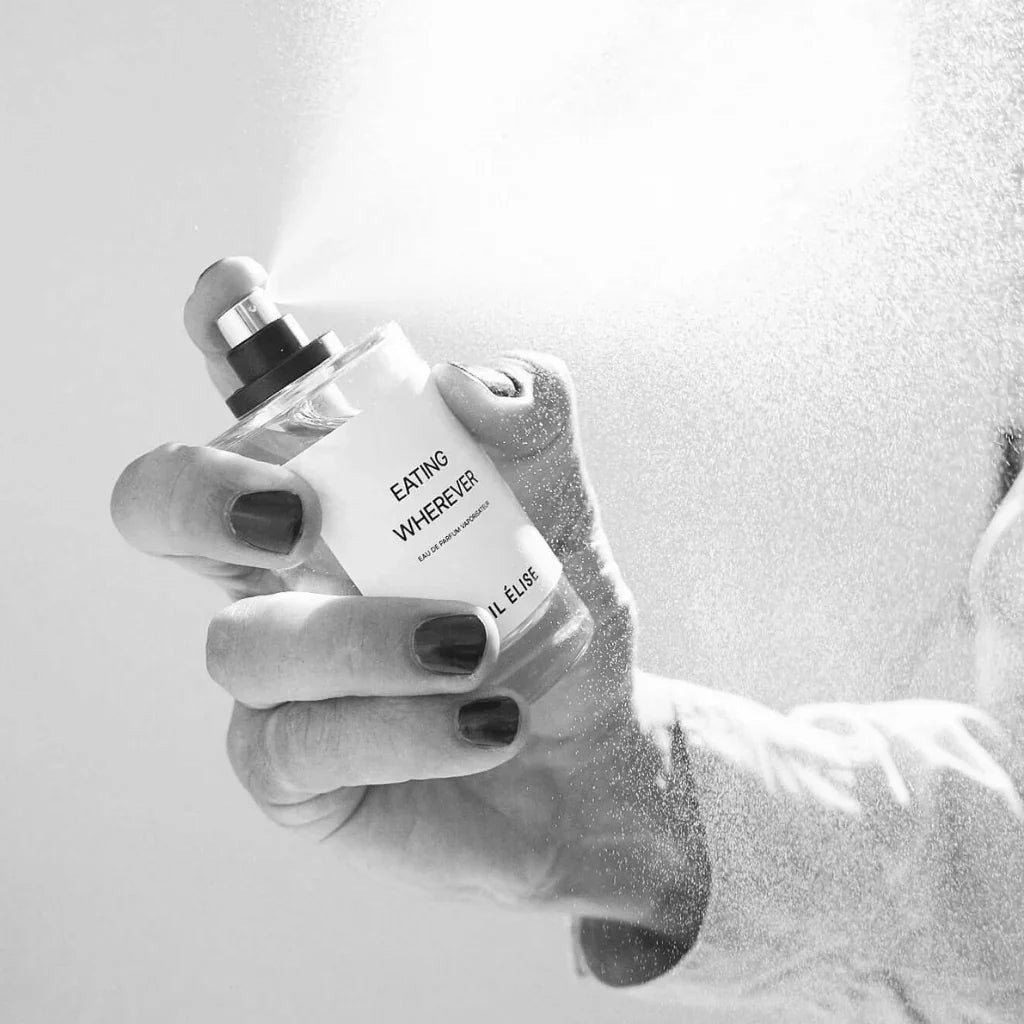 Hand hält einen Sprühflakon mit der Aufschrift "Eating Wherever" von Emil Élise, aus dem Nebel versprüht wird.