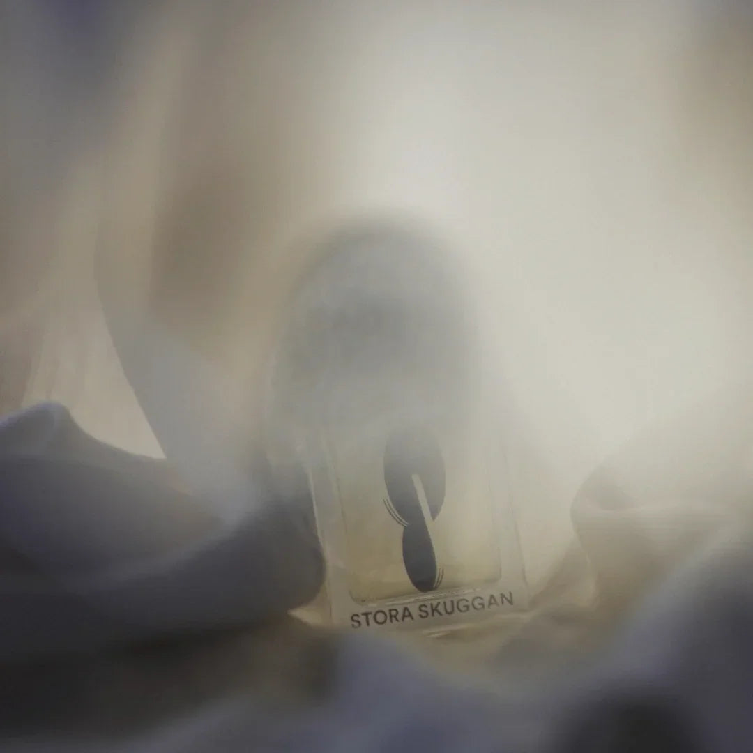 Flakon des Parfüms "Moonmilk" von Stora Skuggan, teils verdeckt von Stoff, mit verschwommenem Licht.