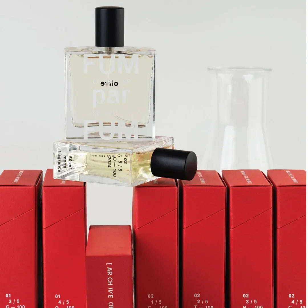 Zwei FUMparFUM L'Artiste Parfumflakons, einer stehend, einer liegend, auf roten Schachteln, mit schwarzem Verschluss.