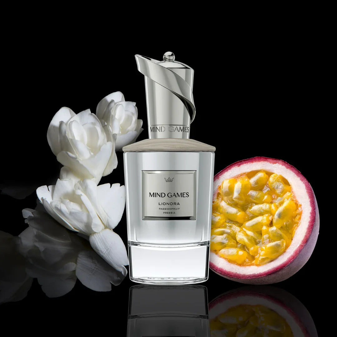 Silberner Parfümflakon "Lionora" von Mind Games mit floralem Design; neben weißen Blüten und aufgeschnittener Passionsfrucht.