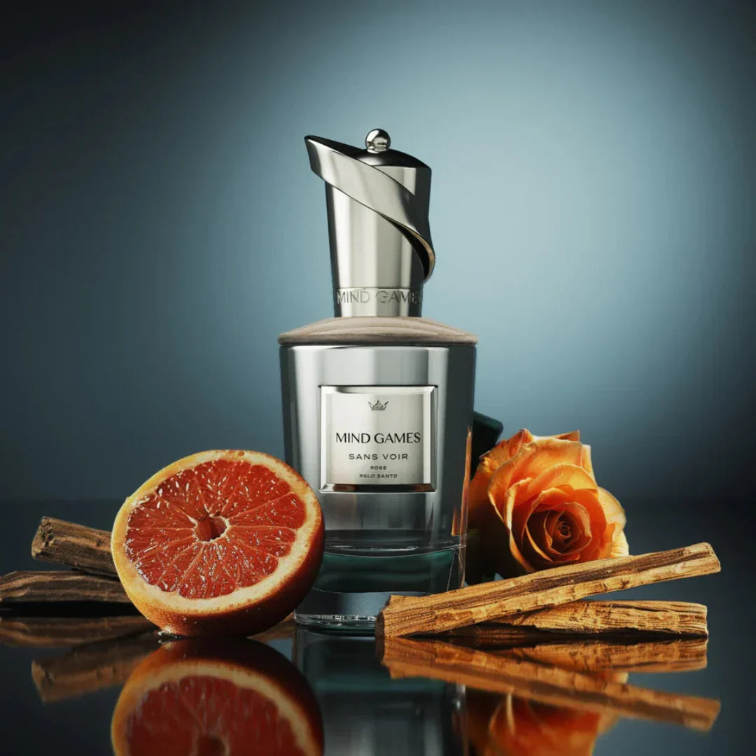 Flakon des Parfums "Sans Voir" von Mind Games mit metallischem Verschluss. Im Vordergrund liegen eine halbe Grapefruit, eine orangefarbene Rose und Zimtstangen.