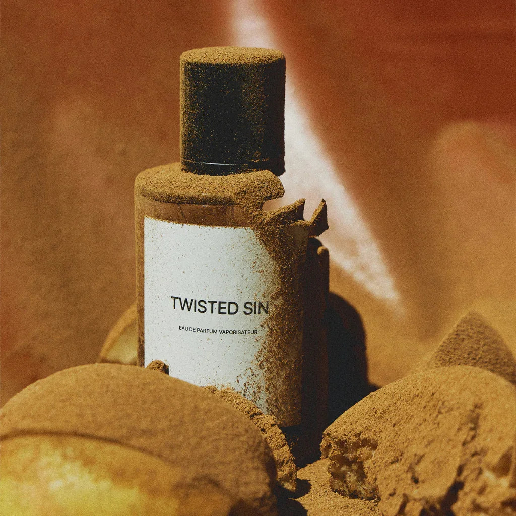 Parfümflasche "Twisted Sin" von Emil Élise, bedeckt mit sandartiger Substanz, schwarzer Verschluss.