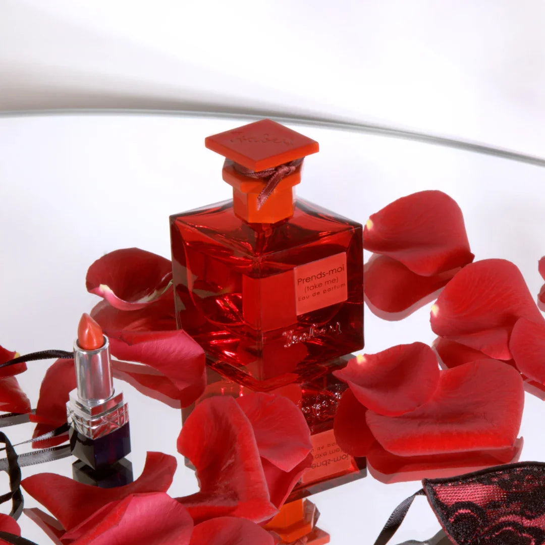 Roter Parfümflakon "Prends-moi" von Isabey mit passendem Verschluss. Umgeben von roten Rosenblättern und rotem Lippenstift.