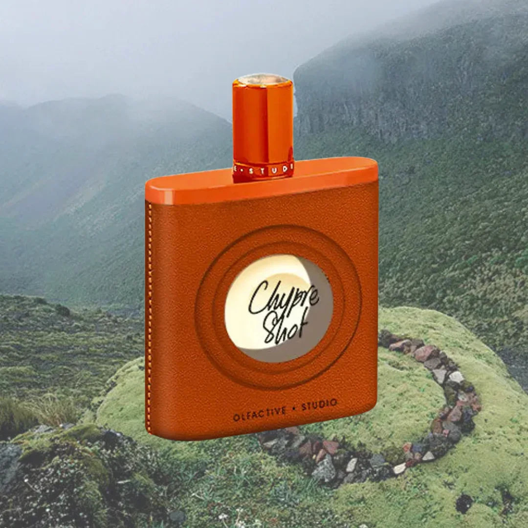 Flakon "Chypre Shot" von Olfactive Studio mit orangefarbenem Verschluss und Lederhülle, umgeben von einer Naturlandschaft.