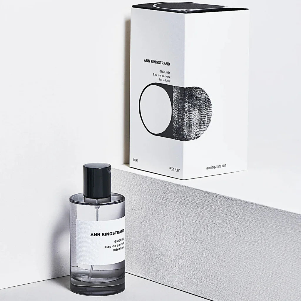 Parfümflasche "Ground" von Ann Ringstrand neben der passenden Produktverpackung, mit schwarzem Deckel und weißem Etikett.
