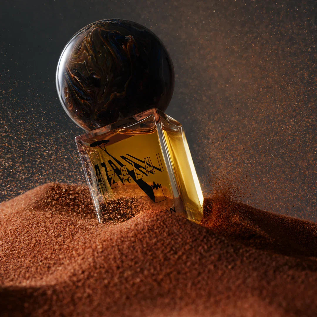 Parfümflasche "Azalai" von Stora Skuggan mit einem kugelförmigen, marmorähnlichen Verschluss, halb im Sand versunken.