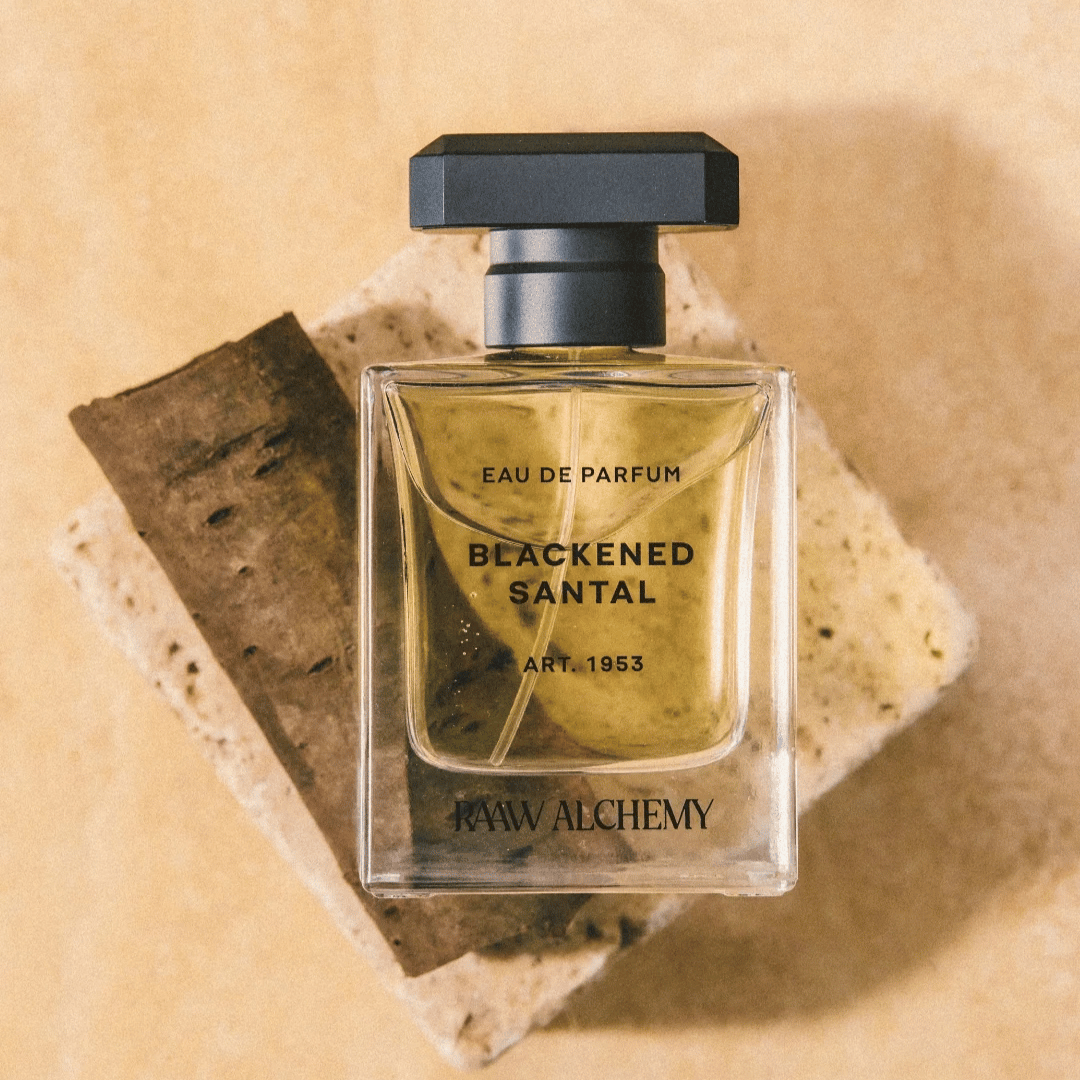 Blackened Santal Nischenflakon liegend auf Travertin von der Marke Raaw Alchemy vor sandfarbenem Hintergrund. Präsentiert beim Fachmann für Nischenparfum scent amor kuratiert von Georg R. Wuchsa