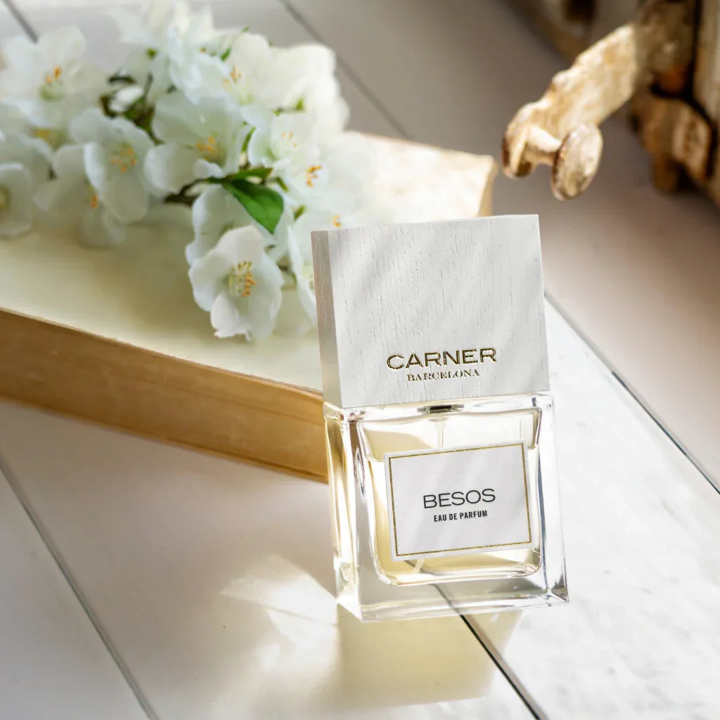Eau de Parfum Besos von Carner Barcelona aus der Love Collection neben Blumen auf ein Buch gelehnt - bei scent amor erhältlich