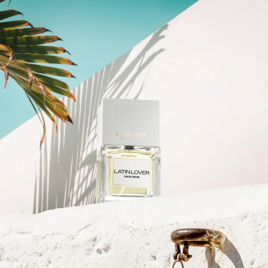 Eau de Parfum Latin Lover von Carner Barcelona aus der Love Collection auf weißem Stein, neben einer Palme - erhältlich bei scent amor