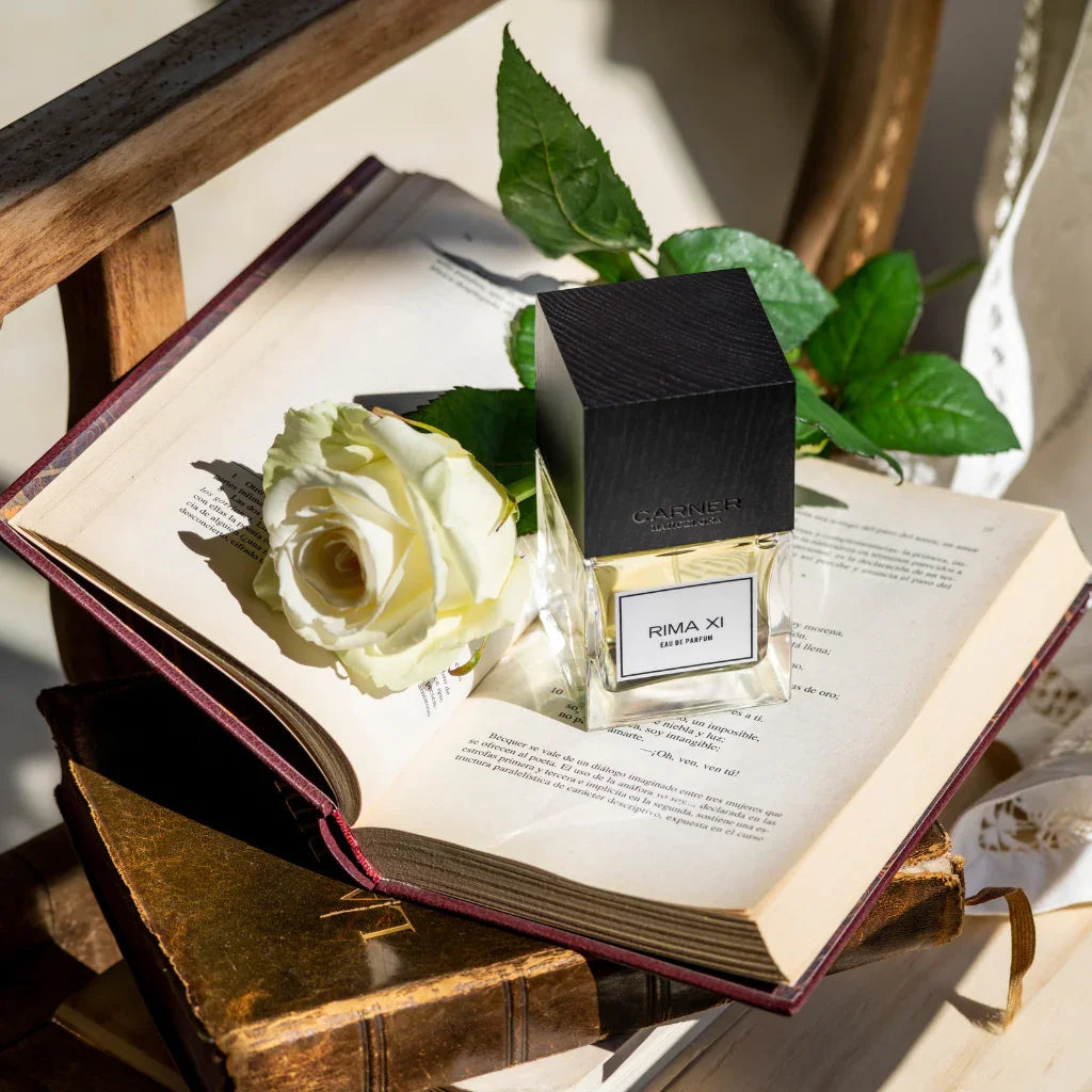 Eau de Parfum Rima XI von Carner Barcelona, Teil der Original Collection, auf einem geöffnetem Buch neben einer weißen Rose - Nischenduft bei scent amor erhältlich