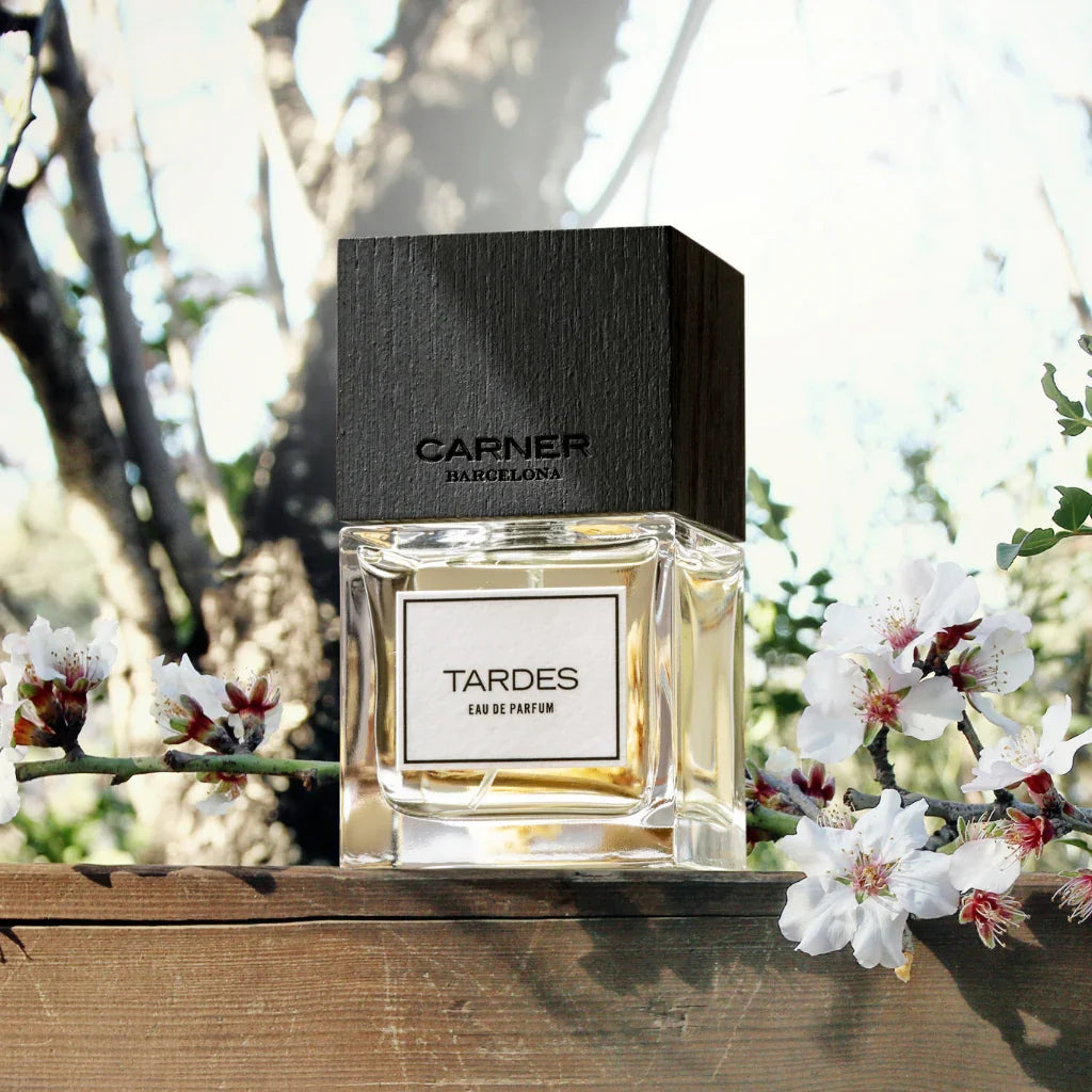 Eau de Parfum Tardes von Carner Barcelona aus der Original Collection vor Blumen und einem Baum im Hintegrund - online bei scent amor verfügbar