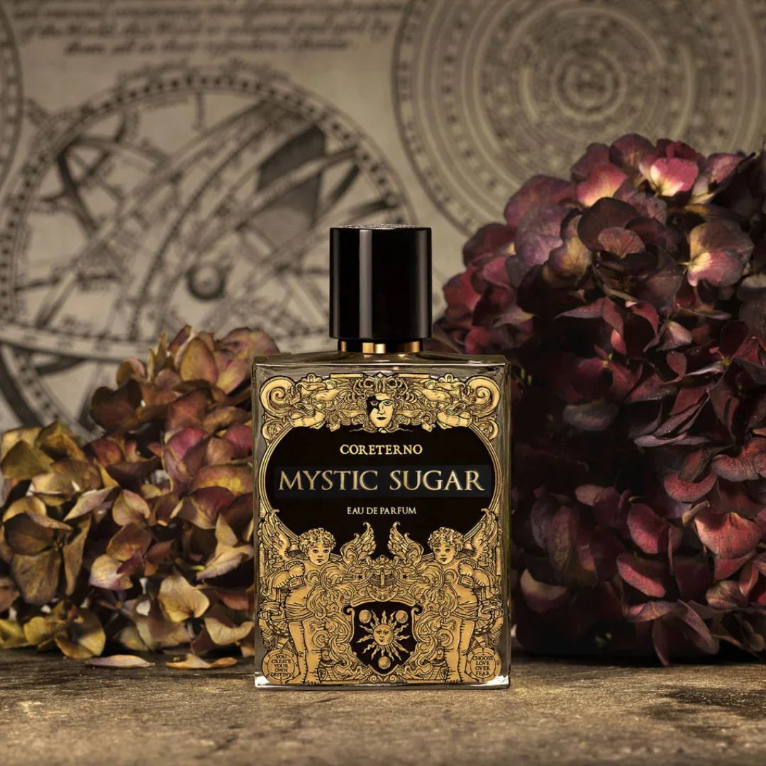 Coreterno Mystic Sugar Eau de Parfum - ein süßer, geheimnisvoller Nischenduft im kunstvollen Flakon vor Blumen, jetzt bei scent amor