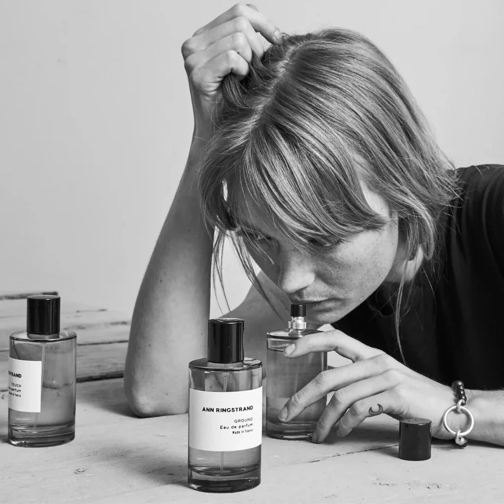 Frau riecht an einem Parfümflakon von "Ground" des Herstellers "Ann Ringstrand". Zwei weitere Flakons stehen auf dem Tisch.