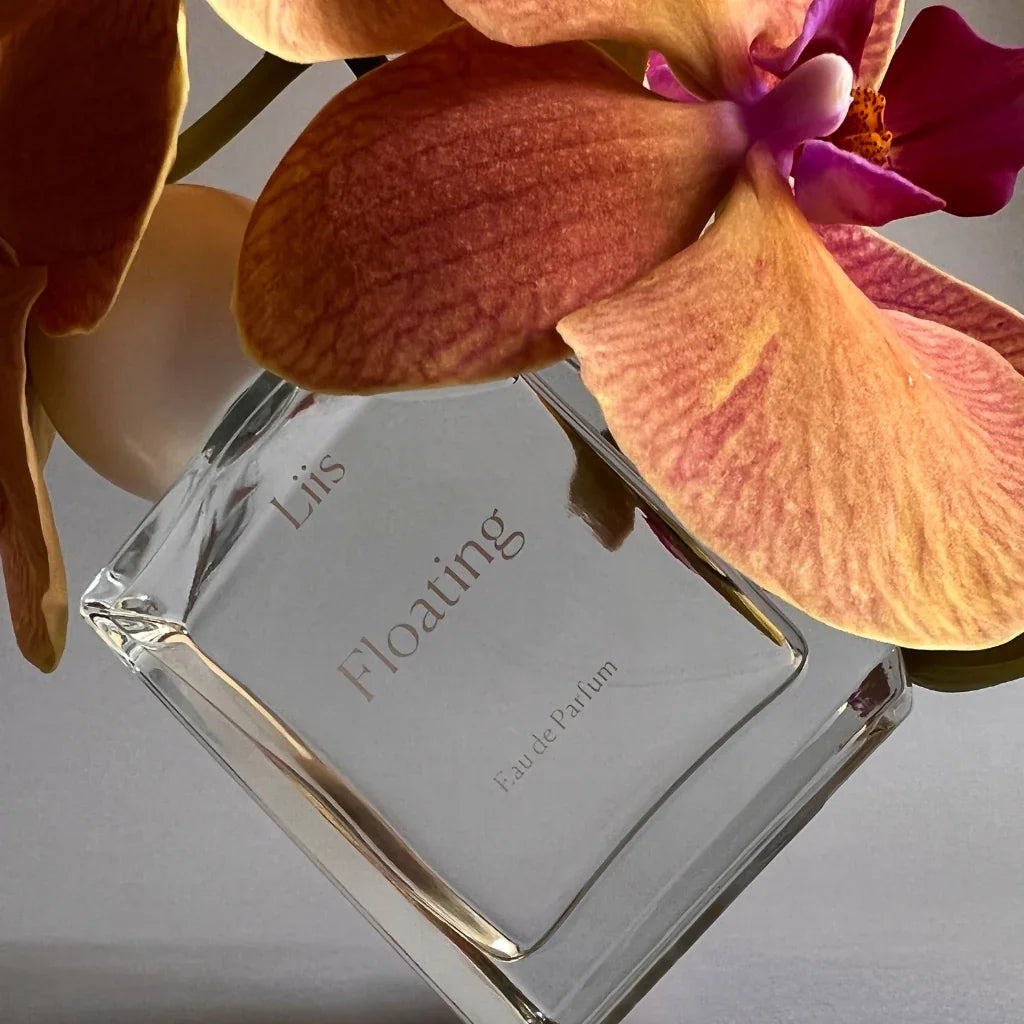 Parfümflakon "Floating" von Liis, transparent, mit floralen Details im Hintergrund.