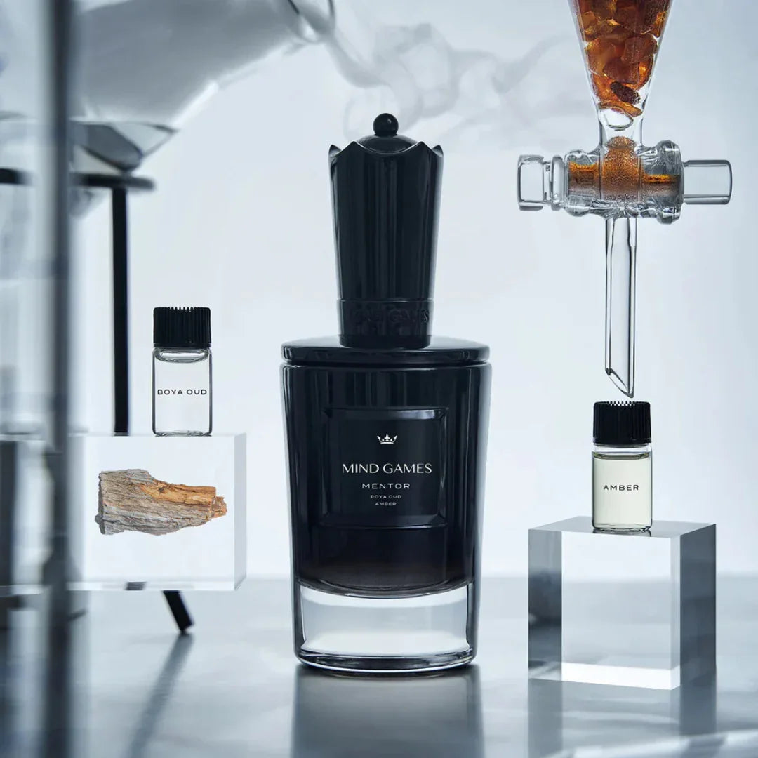 Schwarzer Flakon des "Mentor" Parfums von Mind Games, flankiert von zwei kleinen Glasfläschchen mit Aufschrift "Oud" und "Amber".