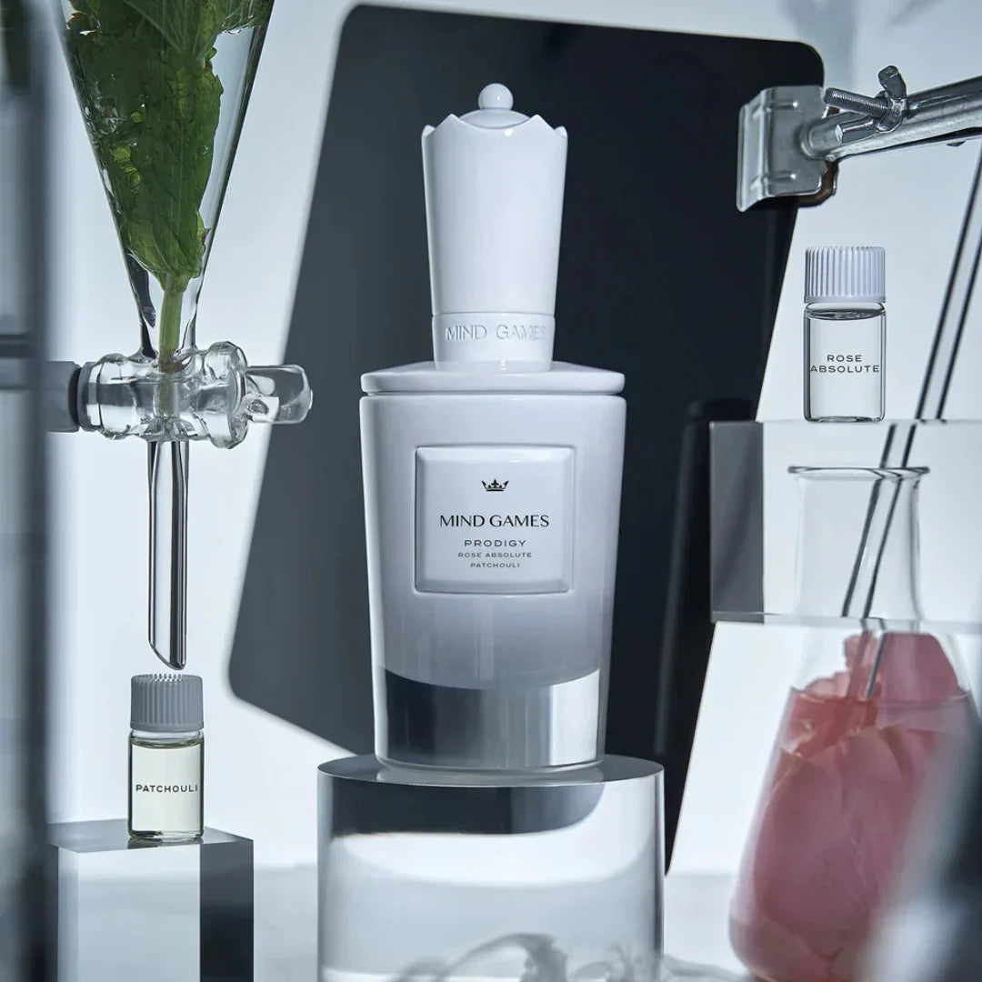 Luxusparfumflakon "Prodigy" von Mind Games in Weiß und Grau mit goldener Schrift umgeben von kleinen Fläschchen.
