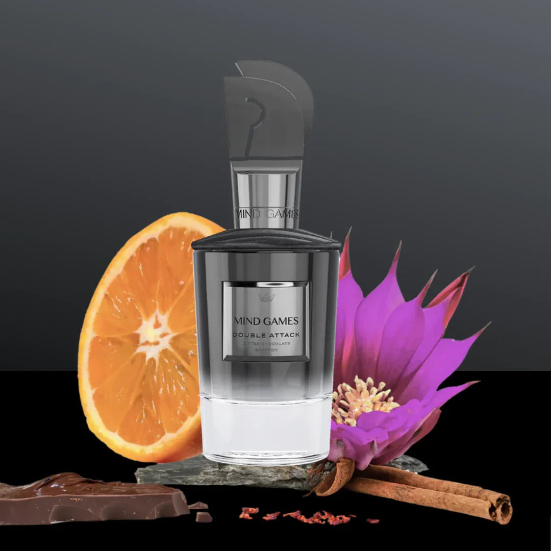 Flakon "Double Attack" von Mind Games, umgeben von einer Orangenscheibe, Zimtstangen, Schokolade und einer lila Blume.