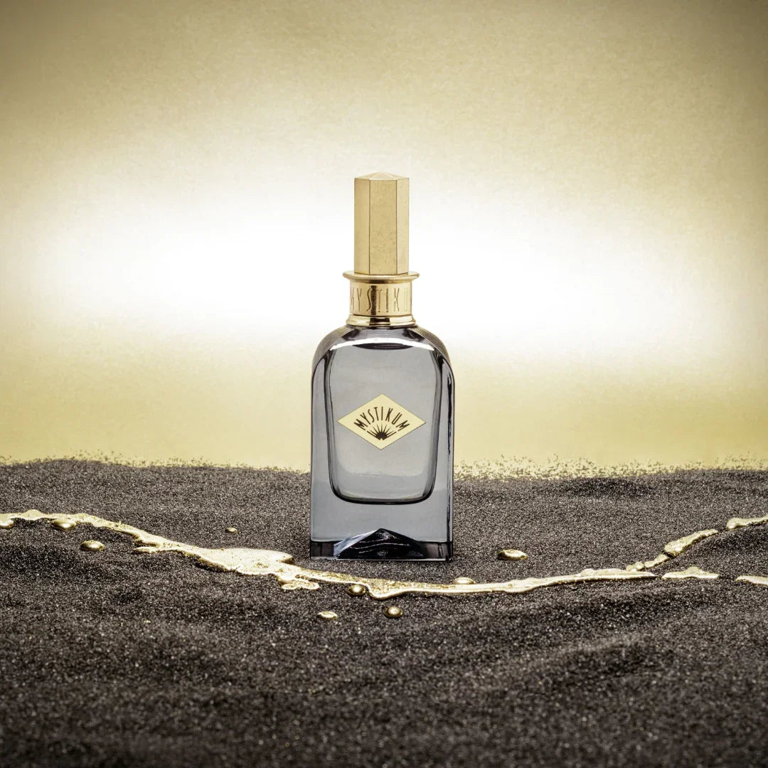 Mystikum Tears on Mystic Sands Eau de Parfum – der Flakon auf dunklem Sand vor goldenem Hintergrund, ein Bild sinnlicher Wärme und orientalischer Noblesse – entdecke es bei scent amor