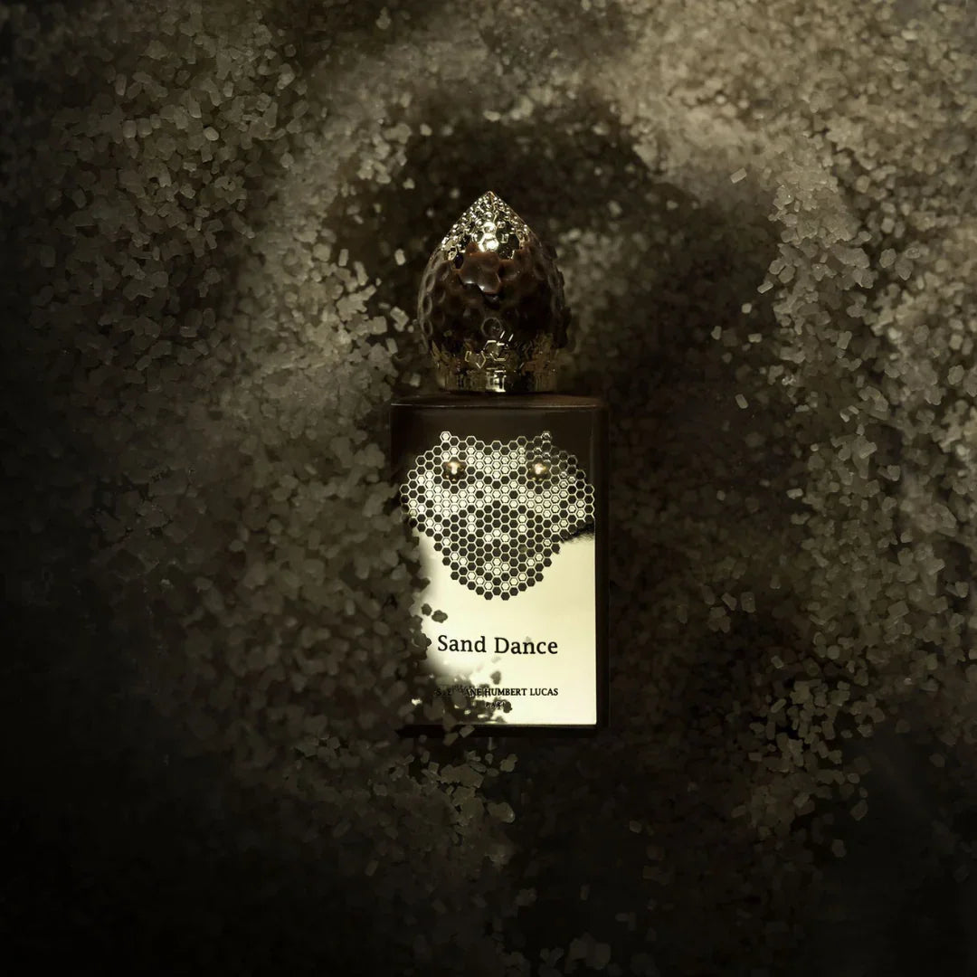 Parfümflasche "Sand Dance" von Stéphane Humbert Lucas, mit runder Kappe und dekorativen Verzierungen, umgeben von Sand bei scent amor