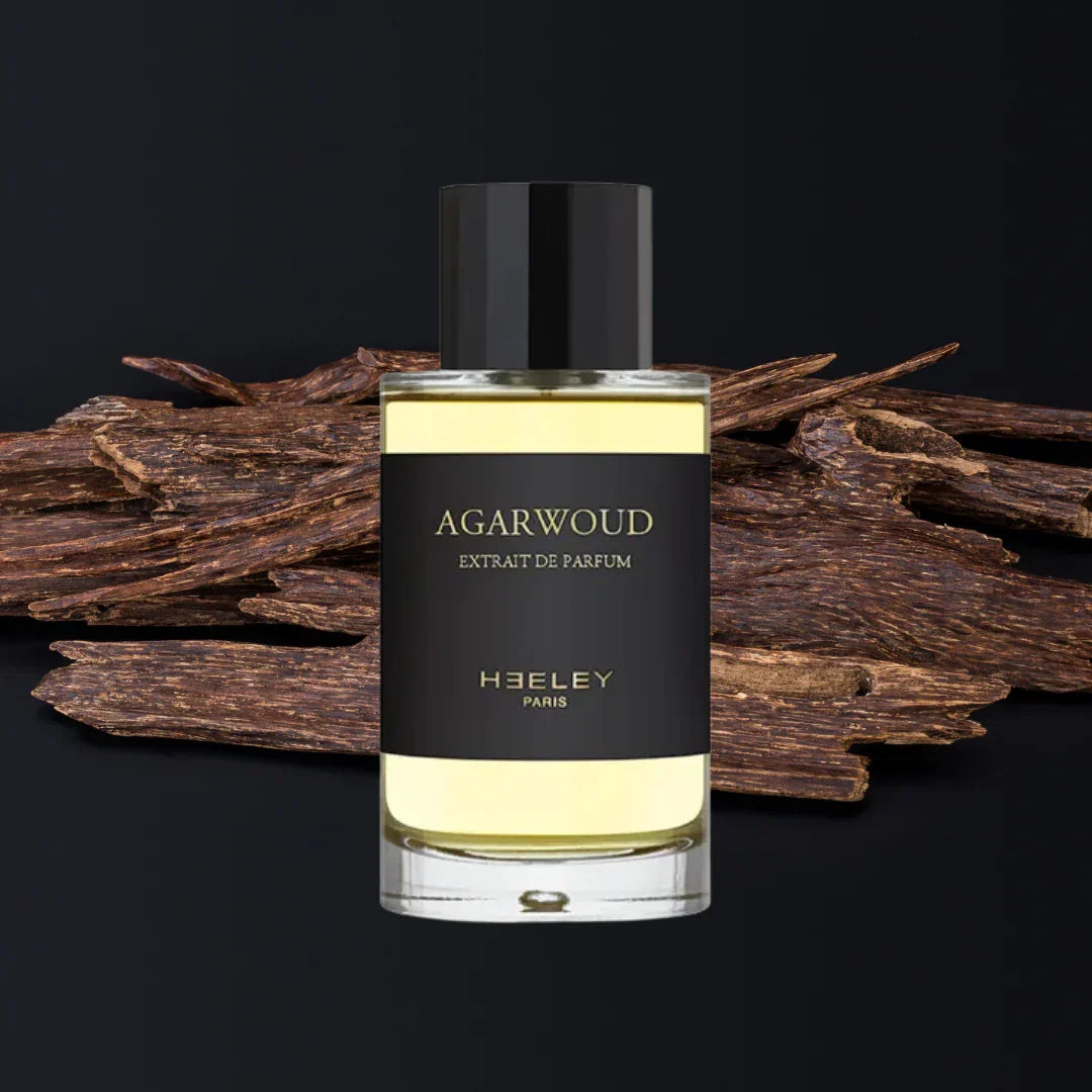 Heeley Agarwoud Parfumflasche mit transparentem Inhalt und schwarzem Etikett, umgeben von Oud-Holzstücken.