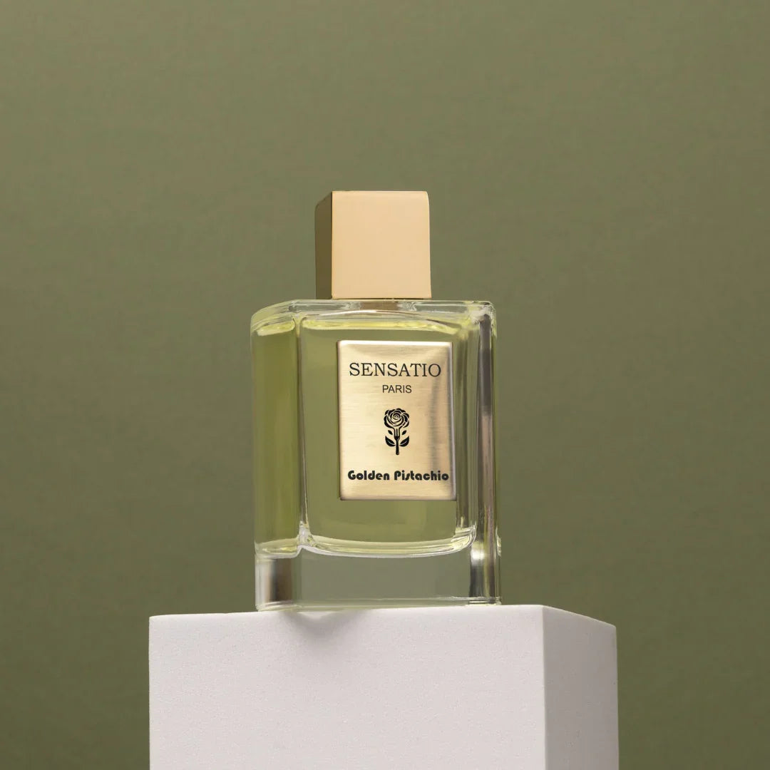 Minimalistisch-goldener Flakon von Sensatio Paris - der elegante Nischenduft Golden Pistachio als Eau de Parfum auf einem weißen Podest mit grünem Hintergrund, auf scent amor erhältlich