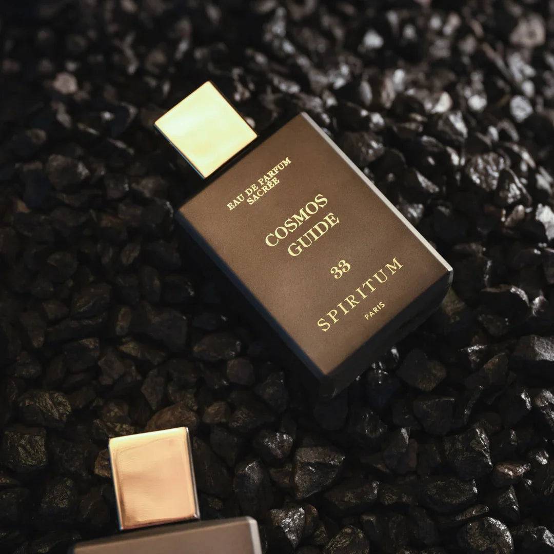 Spiritum Paris COSMOS GUIDE Eau de Parfum – der Flakon liegt schräg zwischen schwarzen Steinen, ein Bild voller Energie und Kontrast, das die kosmische Aura des Dufts spiegelt – erlebe ihn bei scent amor
