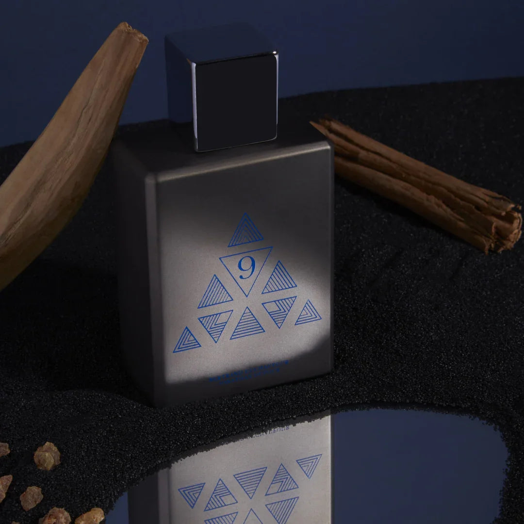 Spiritum Paris FINAL SPIRIT Eau de Parfum – der Flakon steht auf einem blauen, spiegelnden Untergrund, umgeben von Holz und schwarzem Sand – entdecke den Nischenduft bei scent amor