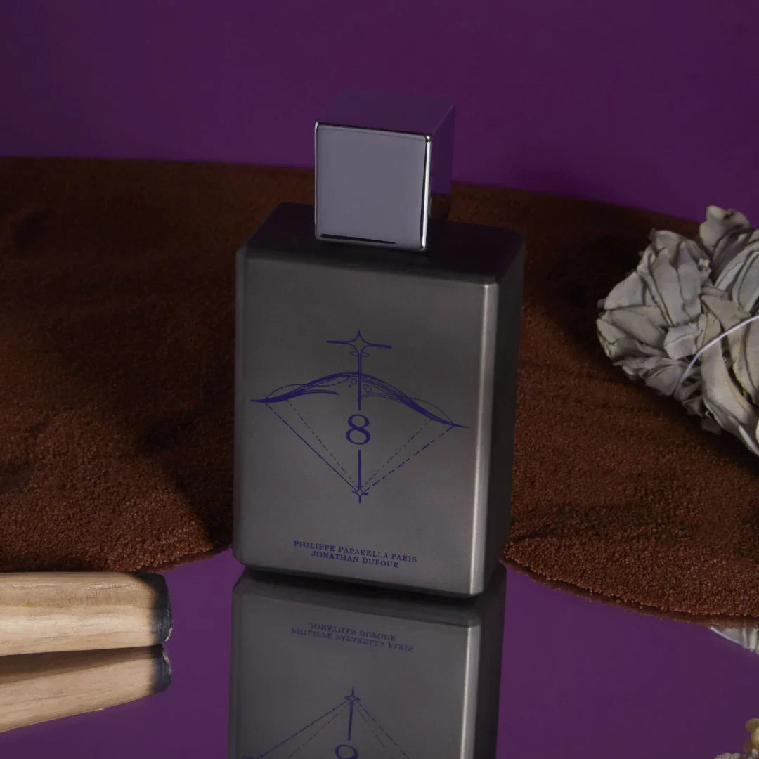 Spiritum Paris MYSTIC WARRIOR Eau de Parfum – der Flakon ruht auf einem gespiegelten, lila Untergrund, umgeben von feinem Sand – ein Bild voller Magie und Kraft, das den geheimnisvollen Charakter des Dufts spiegelt – erlebe es bei scent amor