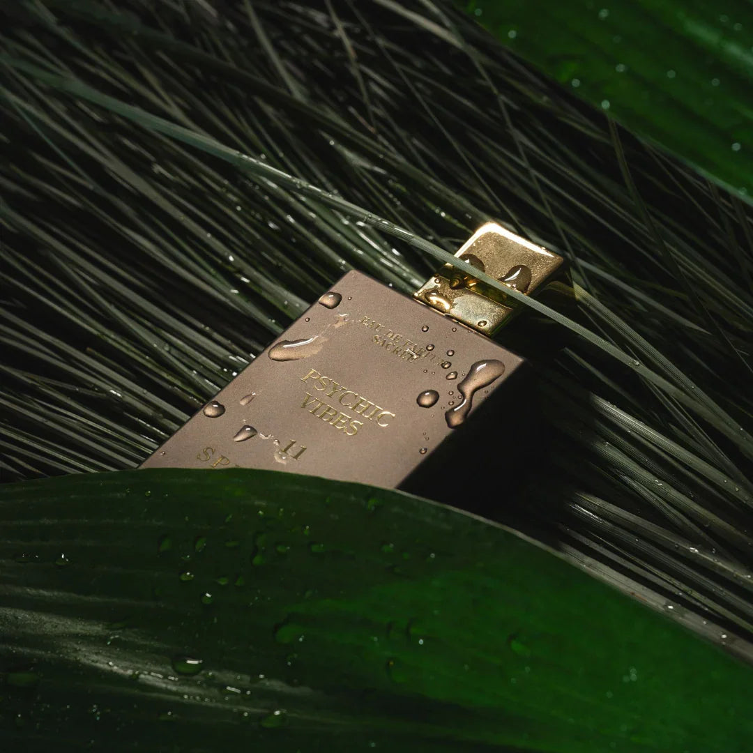 Spiritum Paris PSYCHIC VIBES Eau de Parfum – der Flakon ruht zwischen nassem Gras und Blättern, eine Szene von ungezähmter Natur und tiefer Erdverbundenheit, die den Duftcharakter atmen lässt – erlebe es bei scent amor
