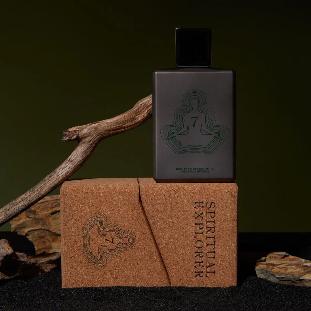 Spiritum Paris SPIRITUAL EXPLORER Eau de Parfum – der Flakon ruht auf einer seitlich liegenden Box, eingebettet in schwarzen Sand und von Holz umrahmt – entdecke es bei scent amor