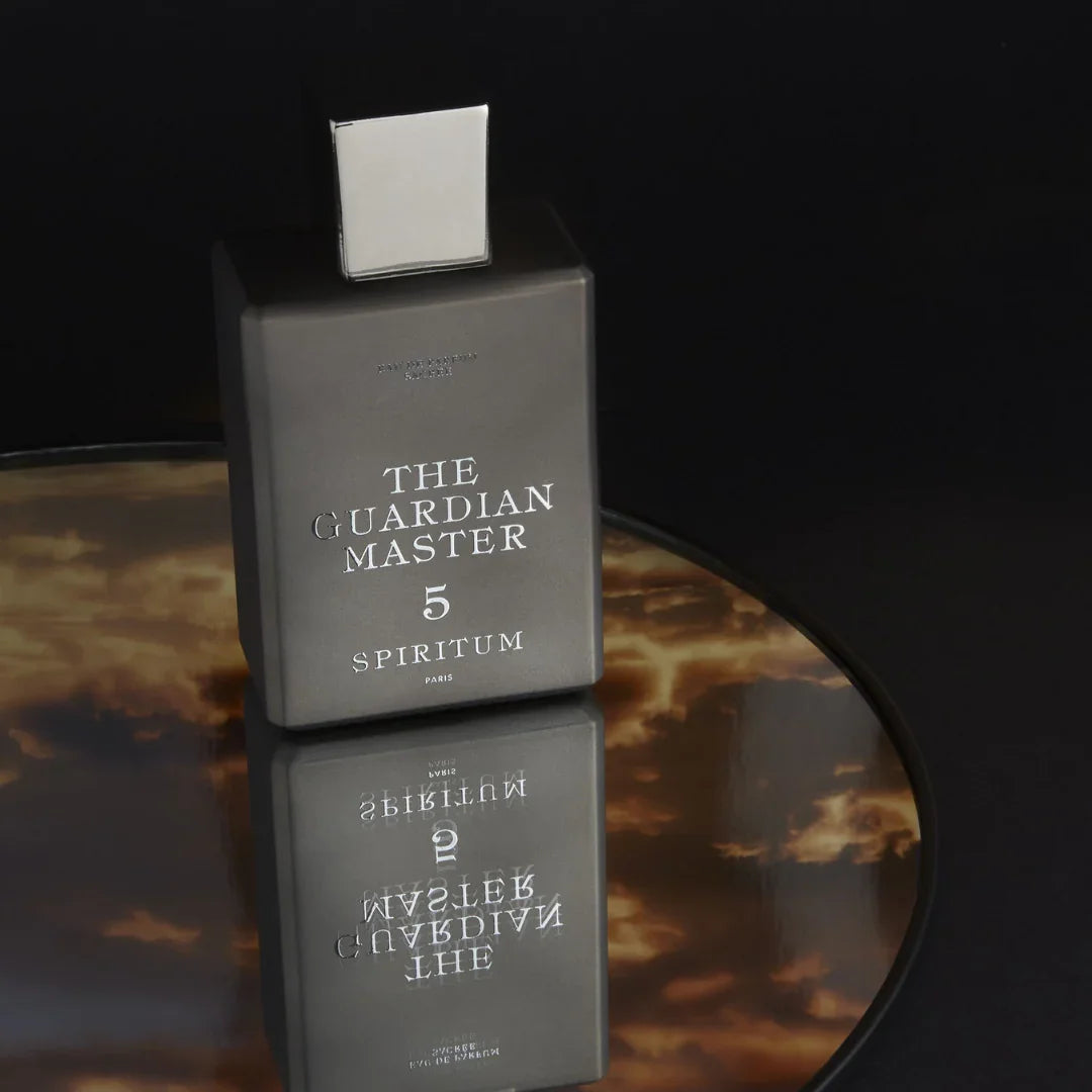 Spiritum Paris THE GUARDIAN MASTER Eau de Parfum – der Flakon ruht auf einem runden Spiegel, während goldene Wolken wie Himmelsboten im Hintergrund schweben – eine visuelle Einladung, den Duft wie ein schimmerndes Ritual bei scent amor zu entdecken