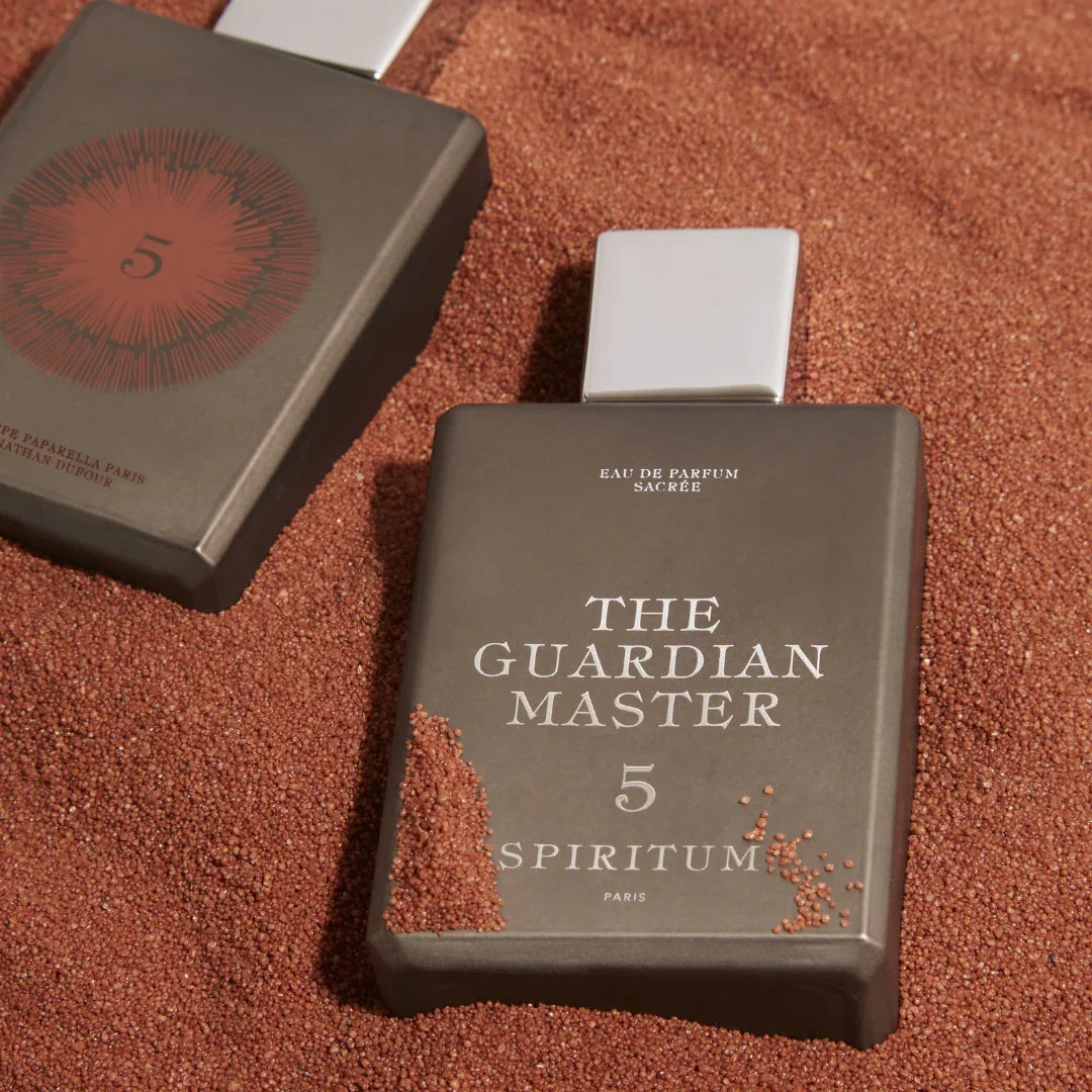 Spiritum Paris THE GUARDIAN MASTER Eau de Parfum – zwei Flakons im braun-goldenen Sand, einer zeigt sein strahlendes Gesicht, der andere das Geheimnis der Rückseite – erlebe es bei scent amor