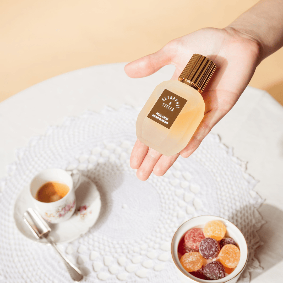 Astrophil & Stella Paris Chéri Extrait de Parfum, Flakon in der Hand gehalten neben süßen Köstlichkeiten, erhältlich bei scent amor