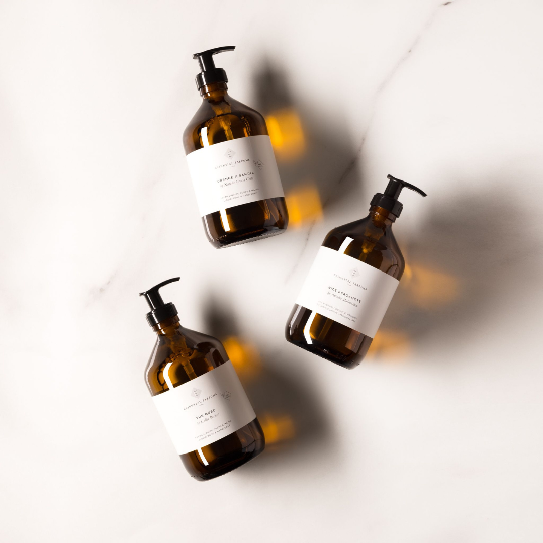 Essential Parfums Liquid Hand & Body Soap, drei braune Pumpflaschen in stilvoller Anordnung auf hellem Untergrund, elegante Präsentation der Duftseifen, erhältlich bei scent amor.