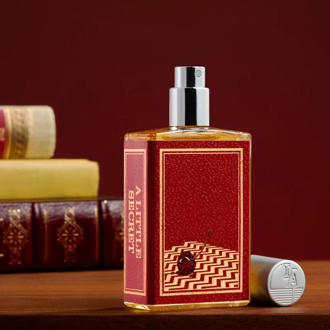 Imaginary Authors A Little Secret Eau de Parfum, stilvoll inszenierter Flakon neben Büchern, warm und literarisch, erhältlich bei scent amor.