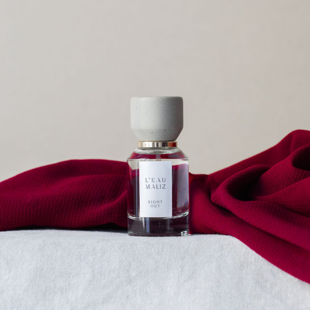 L’Eau Maliz Night Out Eau de Parfum, Flakon inszeniert mit rotem Stoff für eine elegante Abendstimmung, erhältlich bei scent amor.