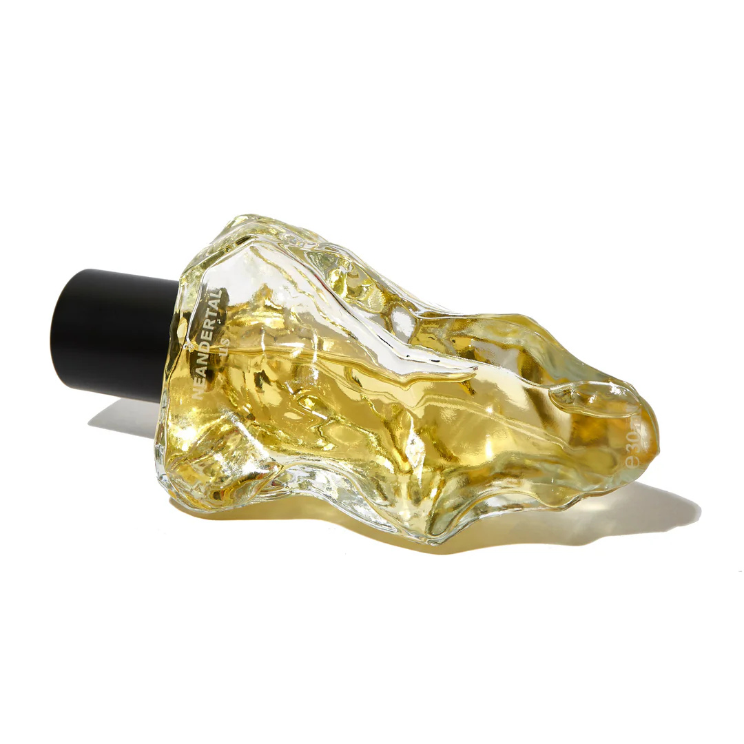 Neandertal us Eau de Parfum, liegender Glasflakon mit fließender Struktur und goldener Flüssigkeit, erhältlich bei scent amor.