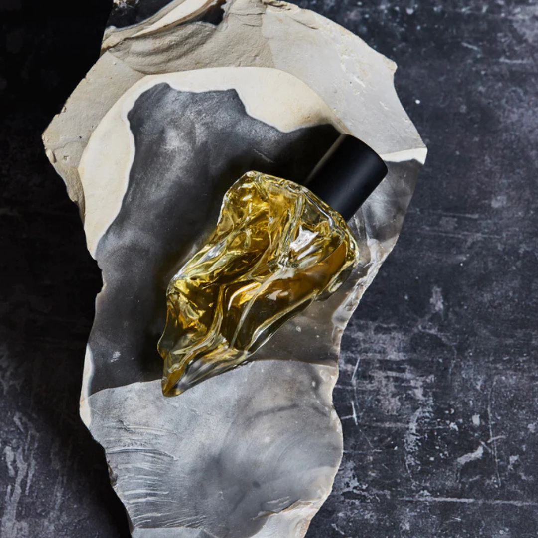Neandertal us Eau de Parfum, organischer Flakon auf Stein platziert, warme Lichtstimmung und mineralische Ästhetik, erhältlich bei scent amor.