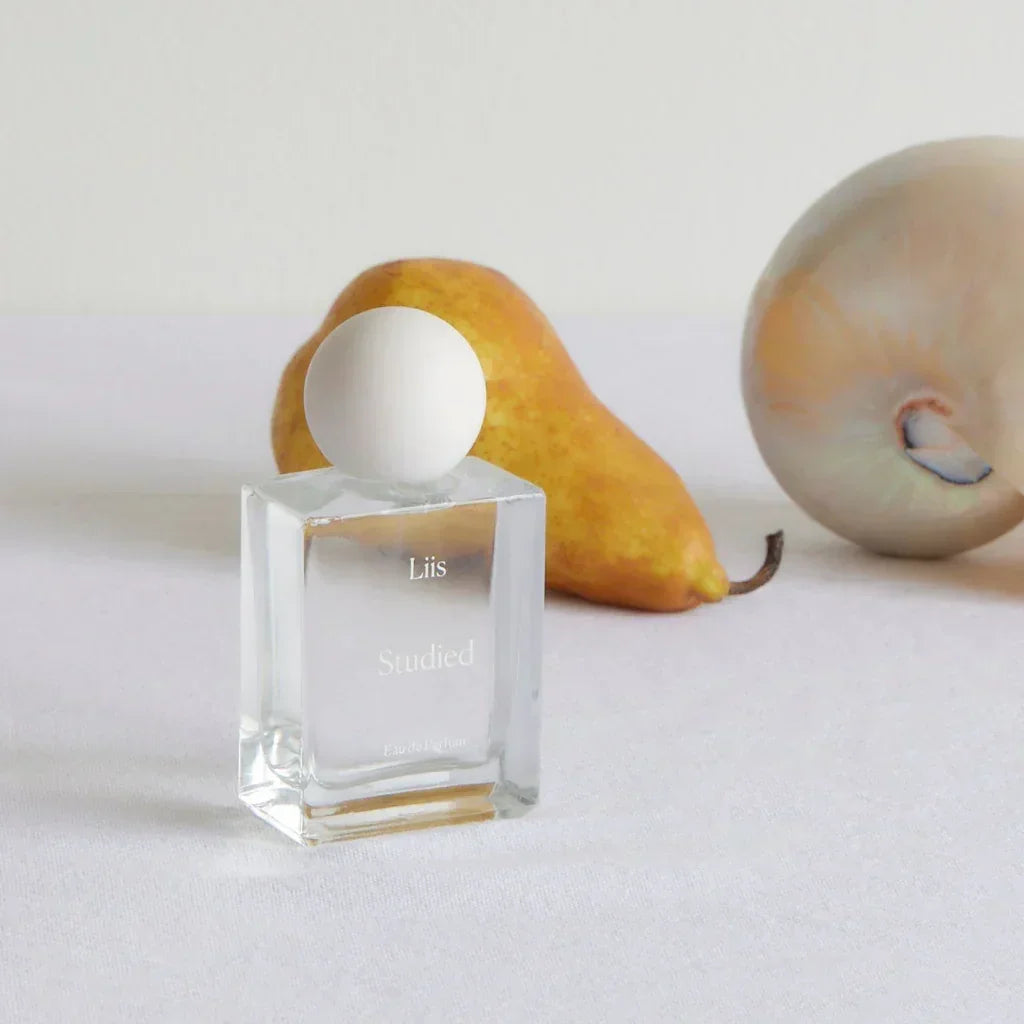 Parfümflasche "Studied" von Liis, rechteckige Glasflasche mit kugelförmigem Verschluss, neben einer Birne.