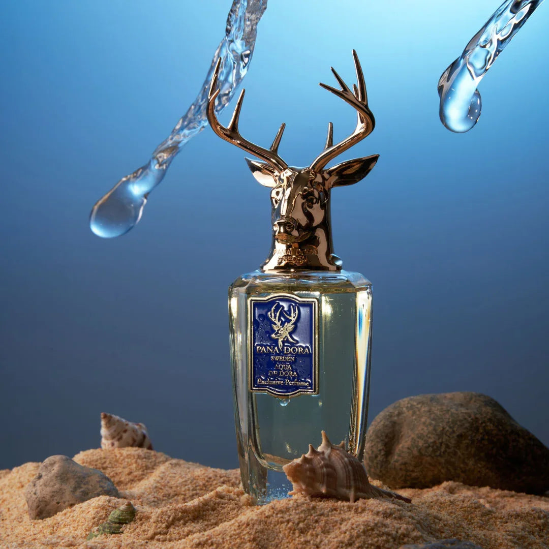 Ein transparentes Parfümflakon mit Hirschkopfverschluss. "Aqua de Dora" von Pana Dora. Tropfen und Sanddekor im Bild.